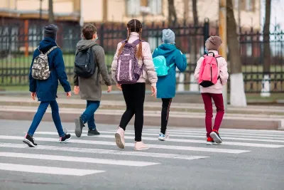 Group of children with backpacks walking across a street at a crosswalk.