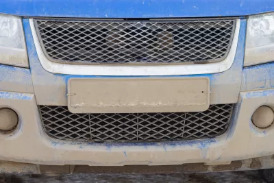 Close-up of license plate on blue car covered in mud, license plate is unreadable.