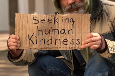 Unhoused man holding sign that reads "Seeking human kindness"