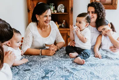 Mother with children sitting next to older woman/grandmother at table.