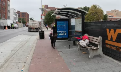 Unhoused person sleeping on bench at bus stop on Baltimore street