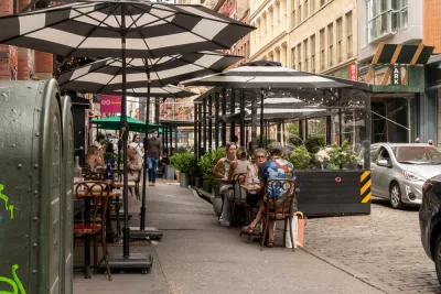 New York City sidewalk with outdoor dining patio with black and white striped umbrellas and black barriers protecting diners from traffic