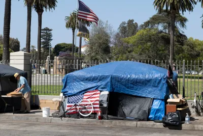 Tent set up on sidewalk covered with blue tarp and American flag on front next to fence to VA campus in West Los Angeles, California.