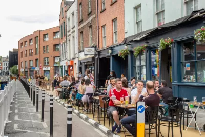 People sitting at outdoor dining tables next to bike lane protected by delineators and three-story buildings in Dublin, Ireland
