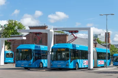 Blue electric transit buses at a charging bay in Gothenburg, Sweden with two-story red brick building in background
