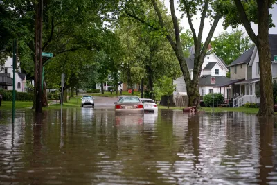 A flooded street in Michigan. A car is driving away from the camera. The water is up past the car's tires.