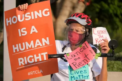 Elderly woman wearing Covid mask holding up "Housing is a human right" sign during tenants' rights protest