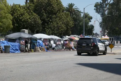 Tents set up by unhoused people on a sidewalk in Los Angeles with a LAPD police SUV passing by.