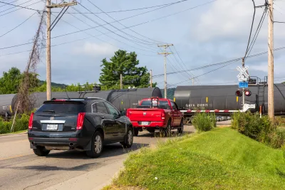 Cars waiting on the road as a train passes a railroad crossing.