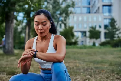 Woman sitting on grass with building in background, looking at her smart watch