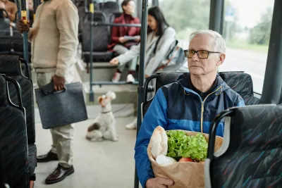 Elderly man holding a paper bag of groceries sitting on public bus.