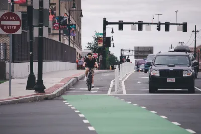 Man riding bicycle in protected green painted bike lane next to black SUV in Boston, Massachusetts.