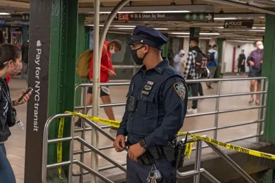Police officer wearing black covid mask stands at top of staircase in New York City subway station.