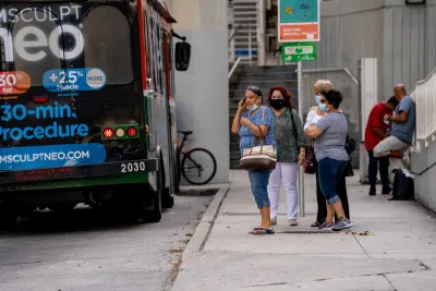 Group of women wearing masks during pandemic era standing at bus stop in Miami.