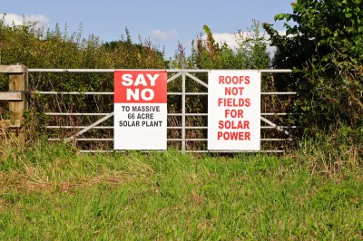 Red and white anti-solar installation signs on farm fence.