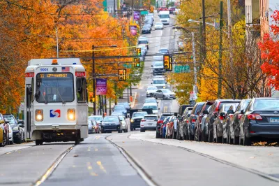 White SEPTA streetcar traveling down wide street in Philadelphia, Pennsylvania with fall foliage on trees on either side of street.