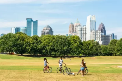 Three people with bikes stopping to chat on grassy field with Atlanta, Georgia skyline in background
