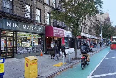 Cyclist rides down green-painted bike lane in Manhattan, New York next to small businesses with colored awnings