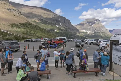 Large group of tourists wait in parking lot in Glacier National Park for park shuttle.
