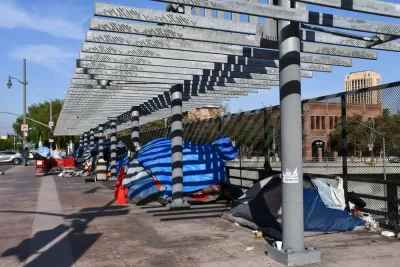 A group of tents inhabited by unhoused people line a freeway overpass in Los Angeles, California