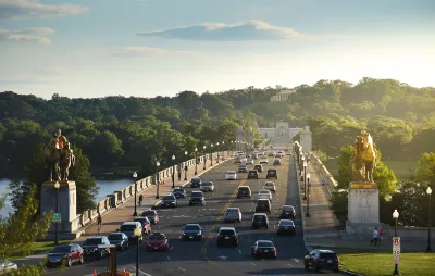 Traffic on the Arlington Memorial Bridge in Washington, DC with neoclassical buildings in background at golden hour.