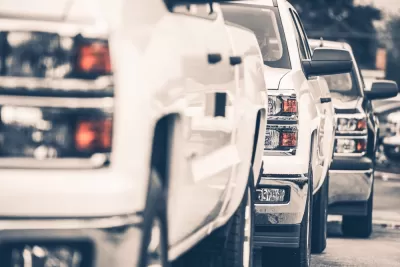 Close-up of white pick-up truck on sales lot from front driver's side; two more trucks behind it