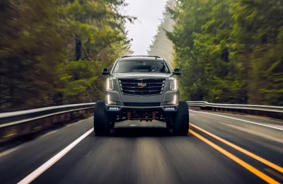 Cadillac Escalade SUV driving toward camera on black asphalt road surrounded by forest