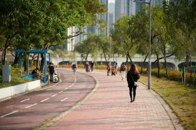 People walking on sidewalk adjacent to bike lane with trees and buildings in background in Hong Kong park
