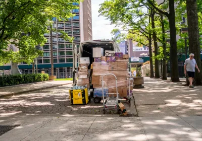 Delivery van parked on street in New York City with lots of packages stacked up outside the back door.