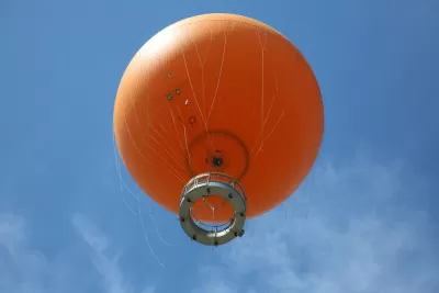 View from below of orange tethered hot-air balloon floating in blue sky