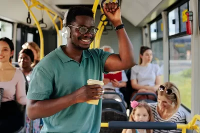 Young man wearing headphones and holding a coffee cup standing on a city bus