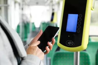 Close-up of person holding up smartphone next to contactless fare reading device on bus