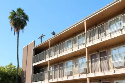 Three-story tan motel building with tall palm tree in the background