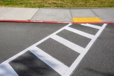 Freshly painted white crosswalk leading to yellow curb cut to sidewalk