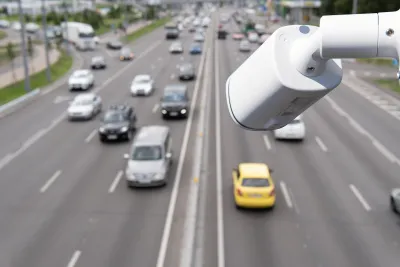 Close-up on white traffic camera installed over a busy roadway.