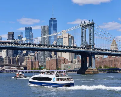 White and blue New York City ferry in river with Manhattan skyline in background.