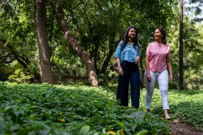 Two women in modern business casual clothing walking through lush green garden or park in Delhi, India.