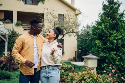African American couple happily looking at each other in front of a two-story house.