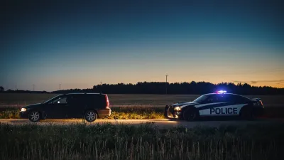 Police car pulling over dark station wagon on rural road at dusk.