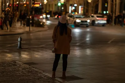 Back view of a woman in hat and coat standing on street in city at night.