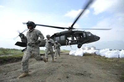 National Guard exiting a Black Hawk helicopter next to a pile of white sandbags during flood relief efforts.