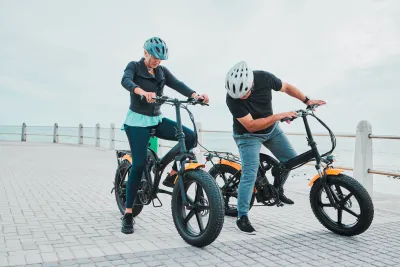 Older couple wearing helmets on electric bikes stopped on a pier next to ocean.