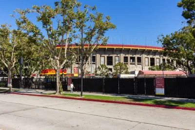 Man walkingon sidewalk in front of Los Angeles Memorial Coliseum sports stadium.
