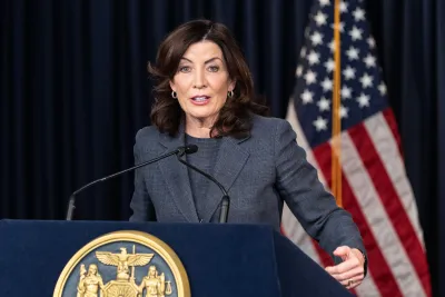 Gov. Kathy Hochul of New York speaking at a podium in front of a dark blue wall and American flag.