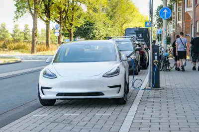 White Tesla plugged into curbside electric car charger on street in Amsterdam, Netherlands.