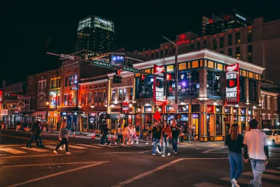 People walking on Broadway street with neon signs for bars and music venues in Nashville, Tennessee.