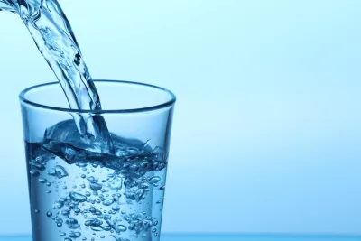Clear glass with water being poured in against blue background.