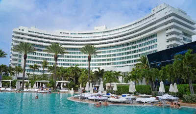 Large white curved hotel building with pool and white poolside chairs and umbrellas in Miami Beach, Florida.