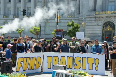 People rallying in front of government building in San Francisco holding "FUND TRANSIT!" sign.