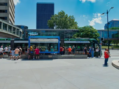 Crowd of people stand at station in front of blue and green Kansas City streetcar.